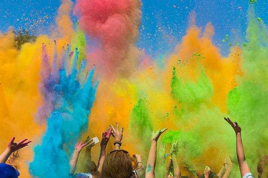 Multidão a atirar pó colorido ao ar, com as mãos levantadas, numa festa Holi