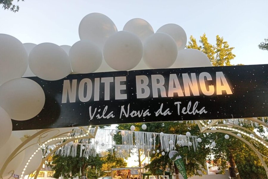 Arco de entrada com balões brancos e a placa "Noite Branca · Vila Nova da Telha", na edição de 2025