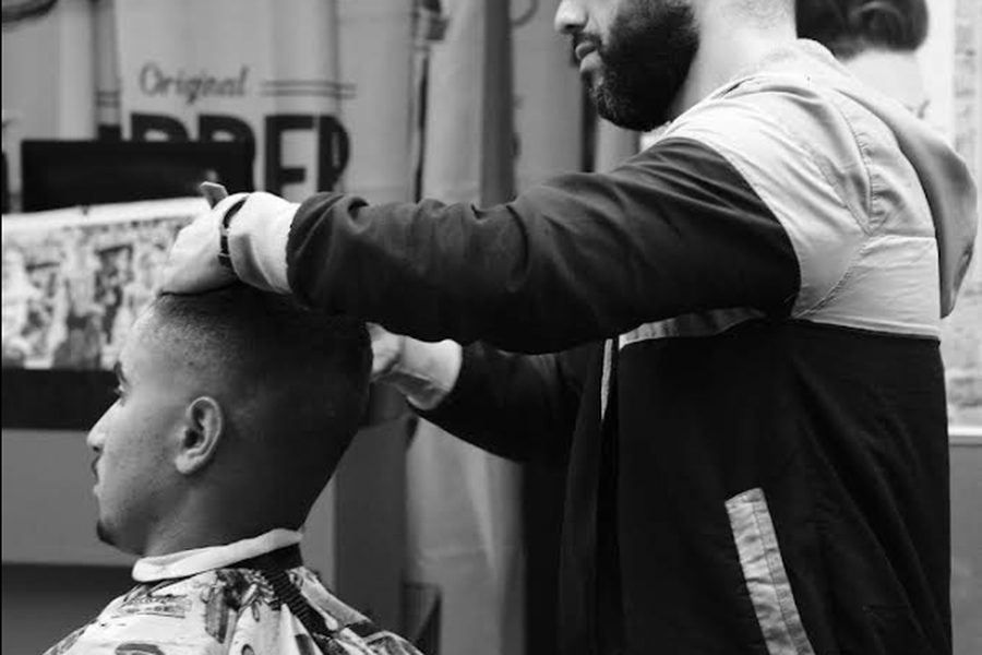 Barbeiro do Big Ben Barbershop a fazer um desenho à máquina atrás da orelha de um cliente