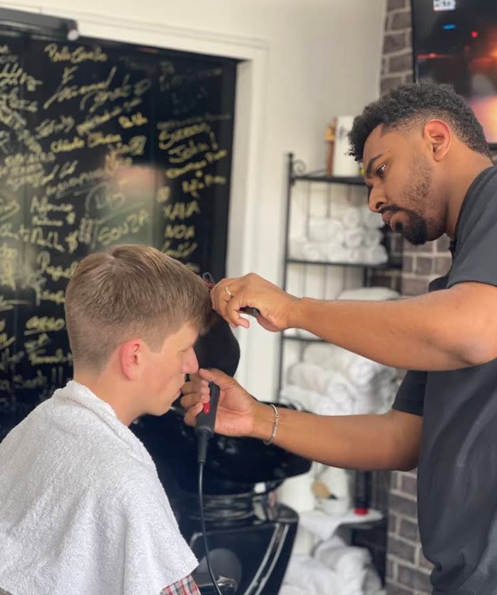 Barbeiro da Big John a cortar o cabelo de um cliente com máquina, junto a um quadro assinado por clientes