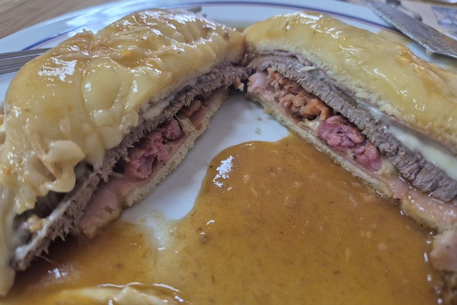 Francesinha do Café Raly cortada ao meio, a mostrar as camadas de fiambre, bife e linguiça debaixo do queijo derretido