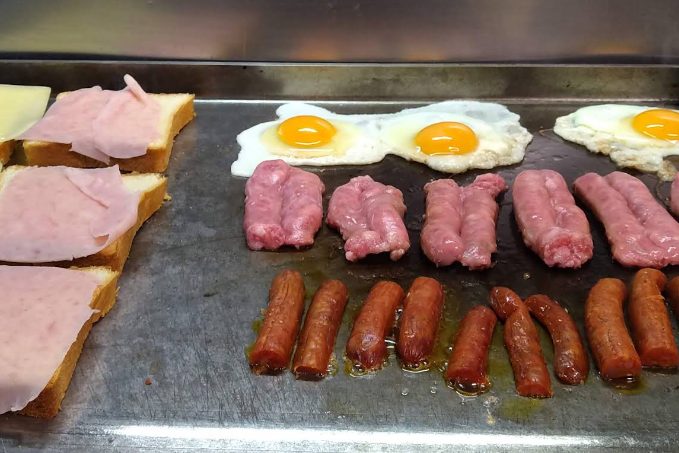 Ovos estrelados, salsichas e sandes de fiambre e queijo a serem preparados na chapa do Café Raly