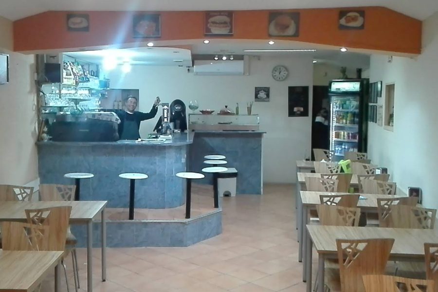 Sala do Café Raly, com balcão em azulejo, bancos altos e mesas de madeira, em Pedras Rubras