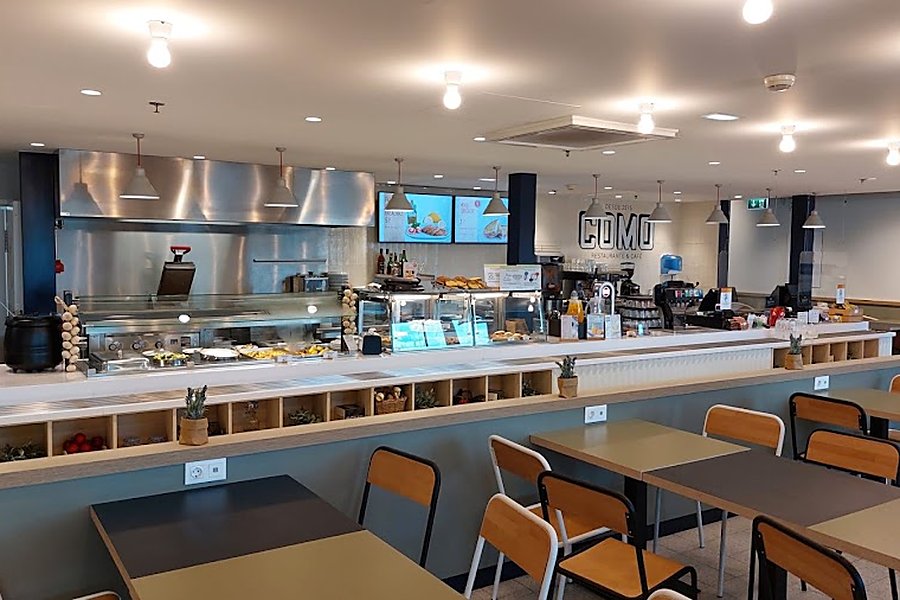 Balcão da cafetaria COMO, no Aeroporto Francisco Sá Carneiro, com o logótipo COMO iluminado e frigoríficos de exposição de sandes, saladas e sumos
