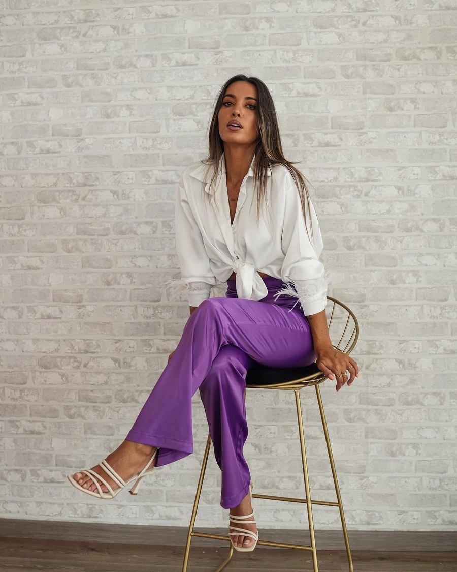 Look da Lady Space: camisa branca de cetim atada à cintura com punhos de plumas e calças largas de cetim roxo, num banco alto dourado