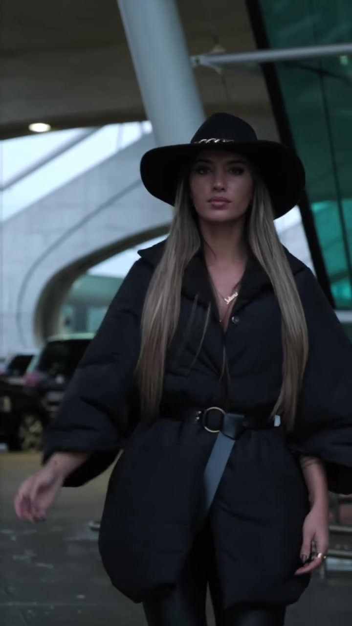 Look total preto da Lady Space: casaco de corte largo com cinto, calças pretas e chapéu de abas largas