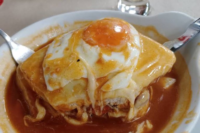 Francesinha com ovo estrelado e molho, servida em prato fundo no Mira Metro