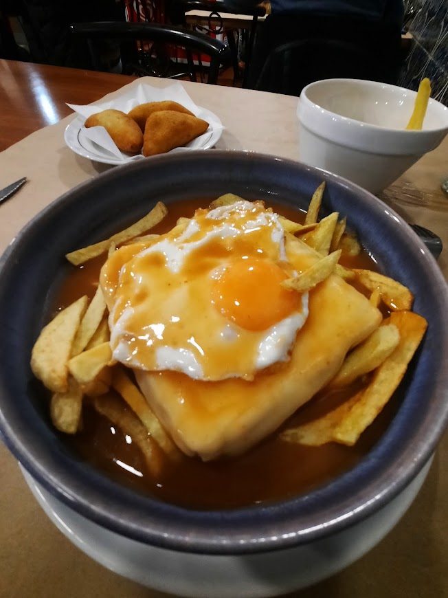 Francesinha com ovo estrelado e batata frita numa travessa funda de molho, no restaurante O Banquinho