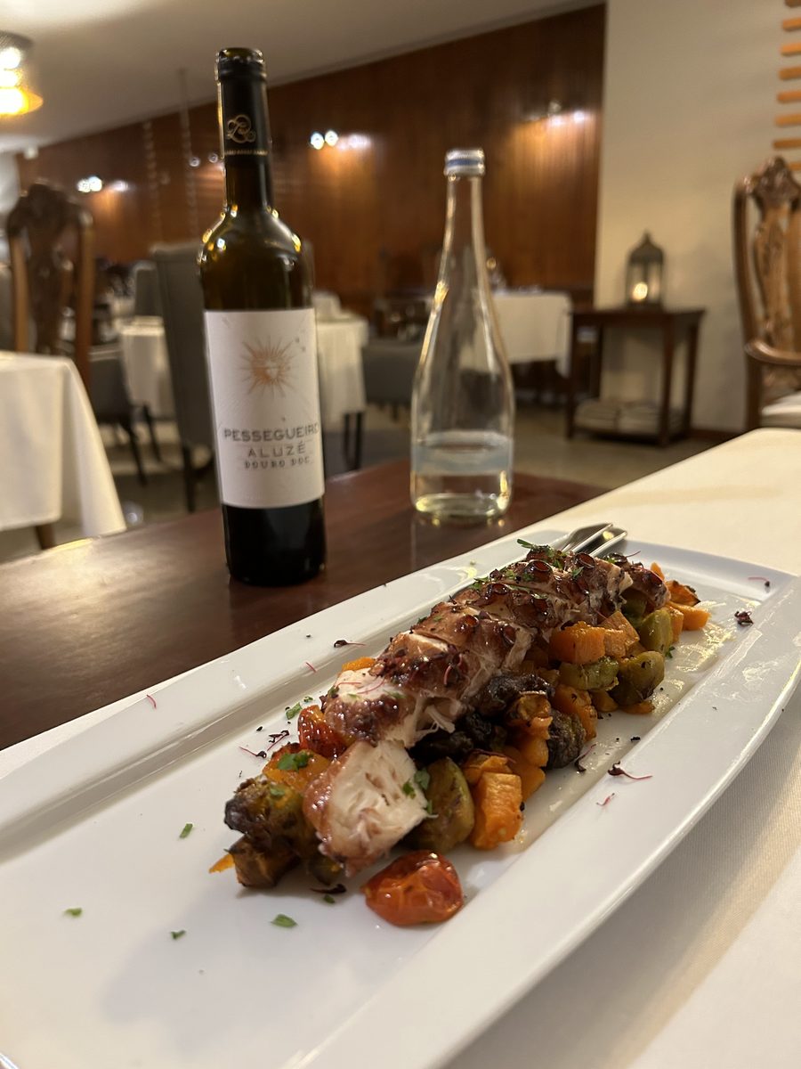 Prato de carne assada com legumes salteados, à mesa com uma garrafa de vinho Pessegueiro Aluzé, no Restaurante O Fernando