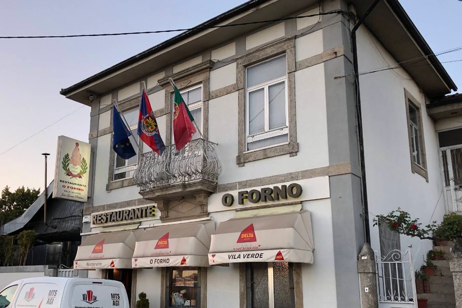Fachada do restaurante O Forno em Pedras Rubras (Maia), com bandeiras, varanda e o letreiro O Forno