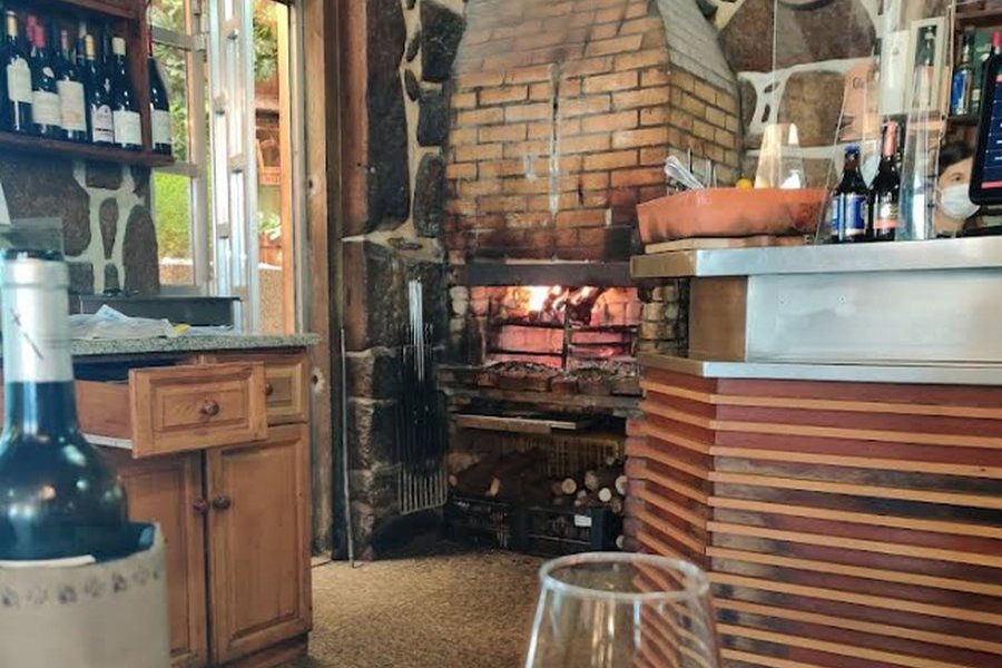 Sala de jantar rústica do O Forno, com lareira de pedra, estante de vinhos antigos e mesas de toalha branca