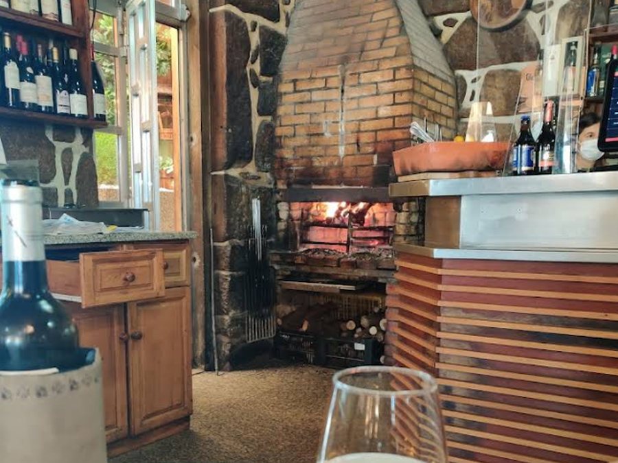 Sala de jantar rústica do restaurante O Forno, em Pedras Rubras (Maia), com lareira de pedra, estante de vinhos antigos e mesas de toalha branca