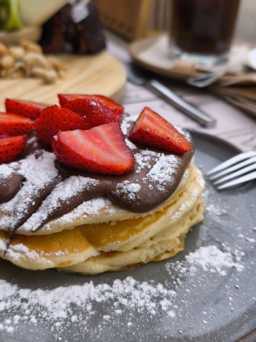 Pilha de panquecas com morangos, creme de chocolate e açúcar em pó, servida n'O Porteiro