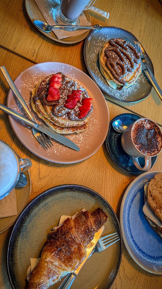 Panquecas com morangos e chocolate, um croissant e cafés numa mesa de madeira d'O Porteiro