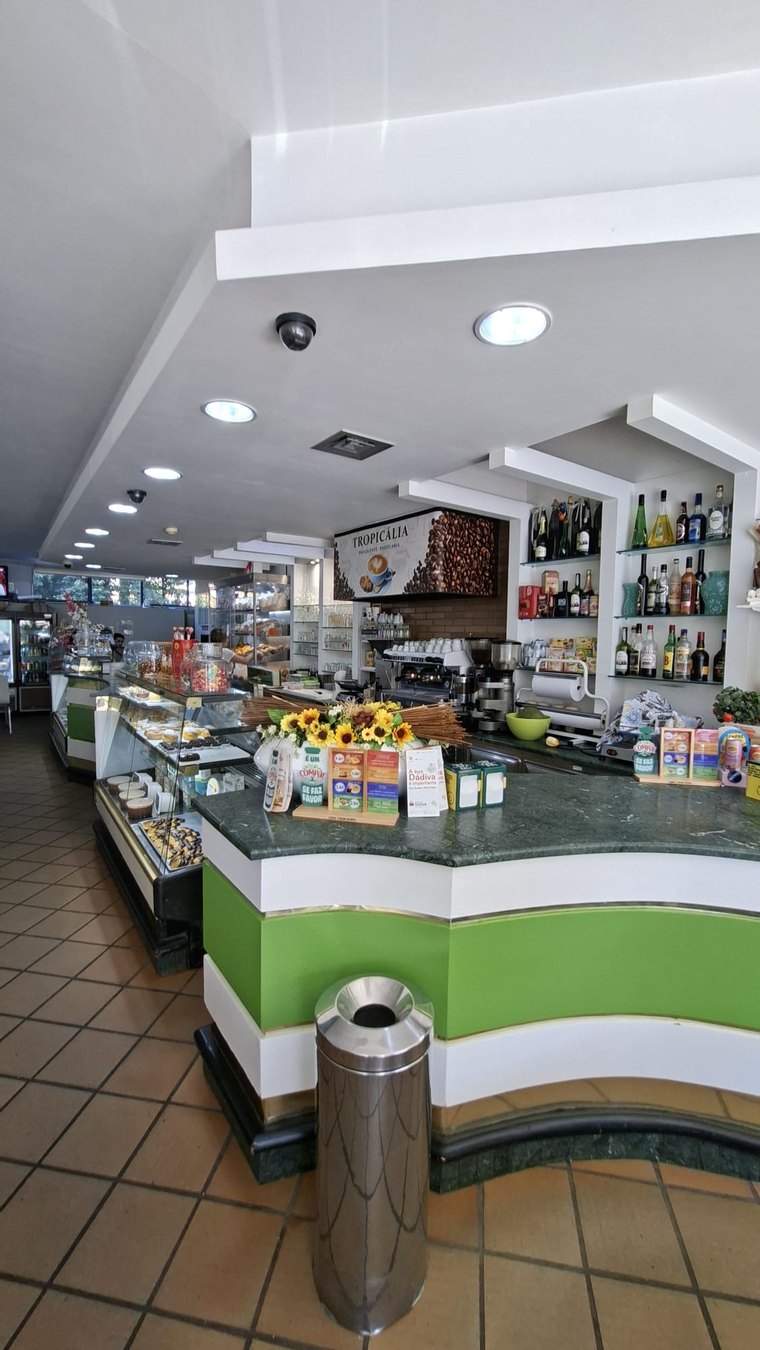 Balcão verde em curva da Tropicália, com tampo de mármore, o letreiro TROPICÁLIA — pão quente e pastelaria, e a máquina de café