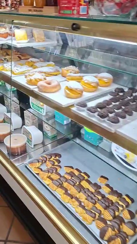 Fotograma da vitrina da Tropicália, com folhados, bolas de Berlim, jesuítas polvilhados e uma fila de bolinhos mergulhados em chocolate