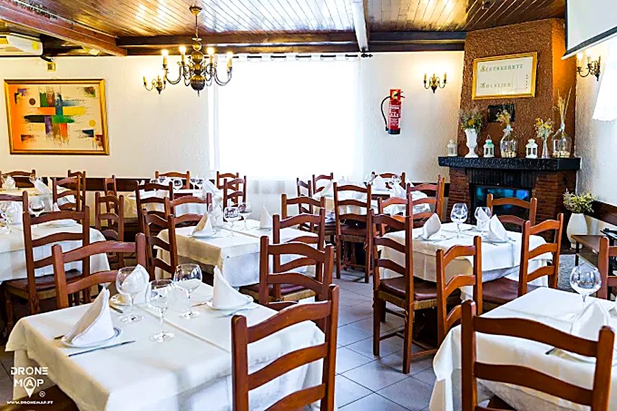 Sala do Restaurante Malheiro, em Pedras Rubras, com mesas postas de toalha branca, cadeiras de madeira e lareira ao fundo