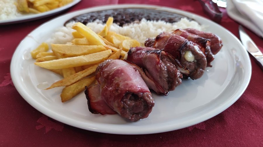 Enrolados de carne envoltos em bacon e recheados de queijo, com batata frita, arroz e feijão preto