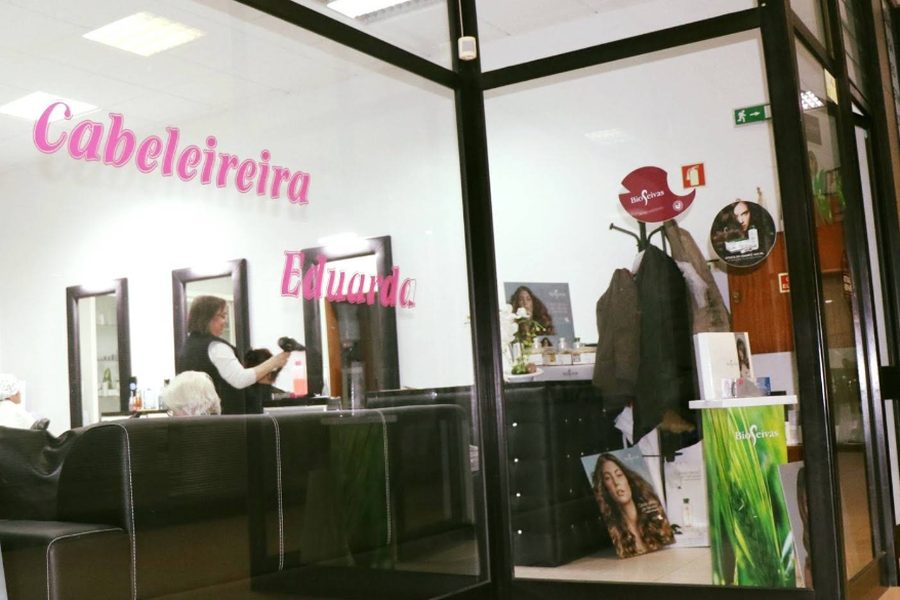 Montra do Salão Eduarda, com o nome no vidro e a cabeleireira a trabalhar, em Pedras Rubras