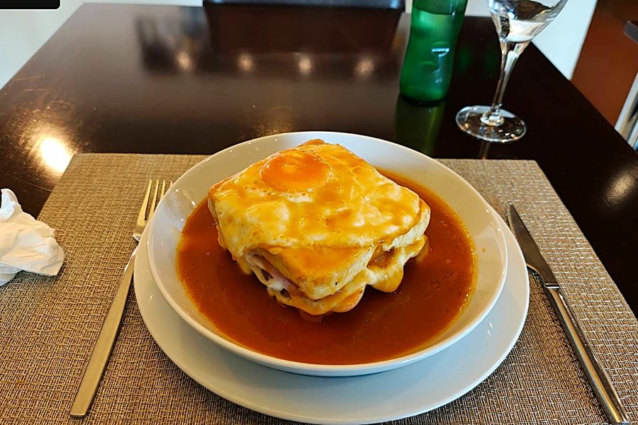 Francesinha do Tomar de Sal, coberta com queijo derretido e ovo estrelado, em prato fundo com molho