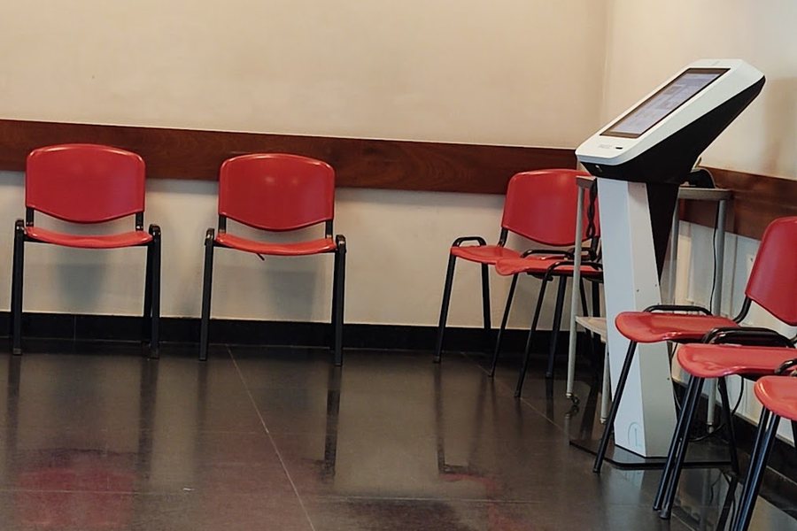 Sala de espera da USF Pedras Rubras, com cadeiras vermelhas, quiosque de senhas e ecrã de chamadas