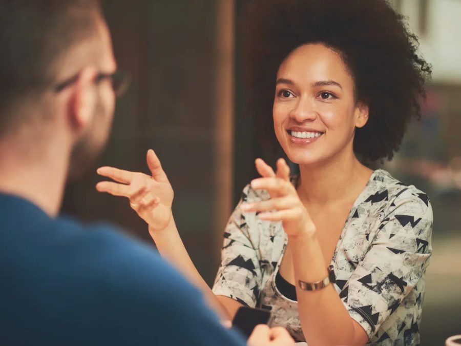 Duas pessoas a conversar de perto, uma delas a gesticular enquanto fala — a aprender uma língua começa por conseguir dizer-se