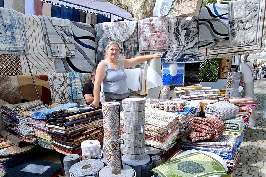 Banca de tapetes e artigos para casa pendurados entre os plátanos