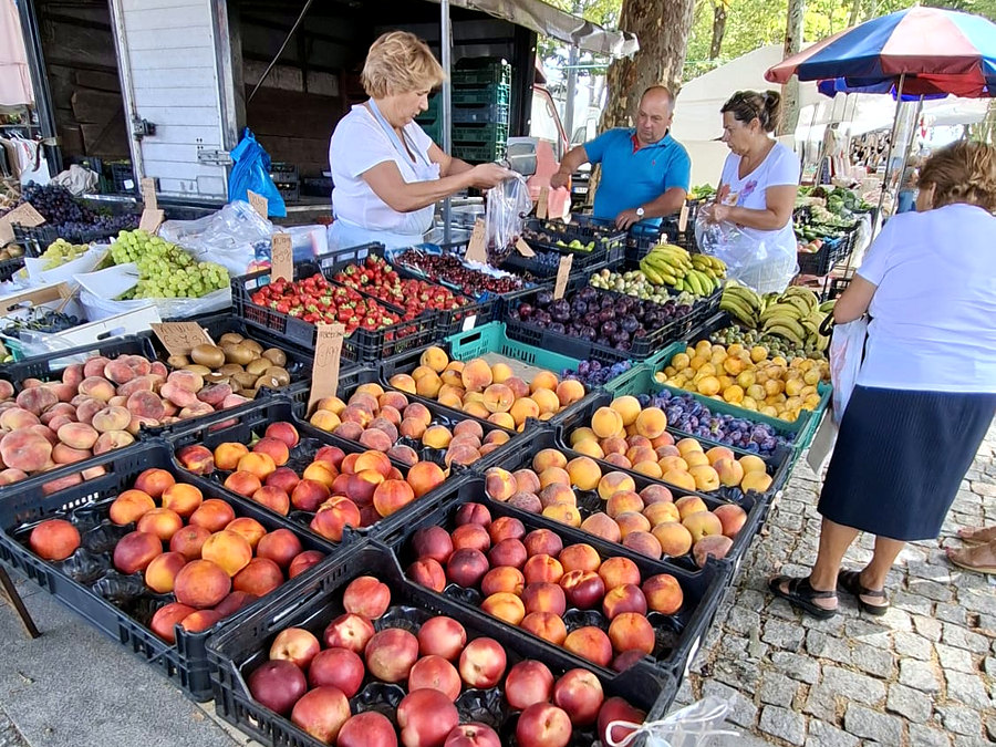 Bancas de fruta na feira de Pedras Rubras — caixas de pêssegos, nectarinas, ameixas e uvas debaixo do toldo