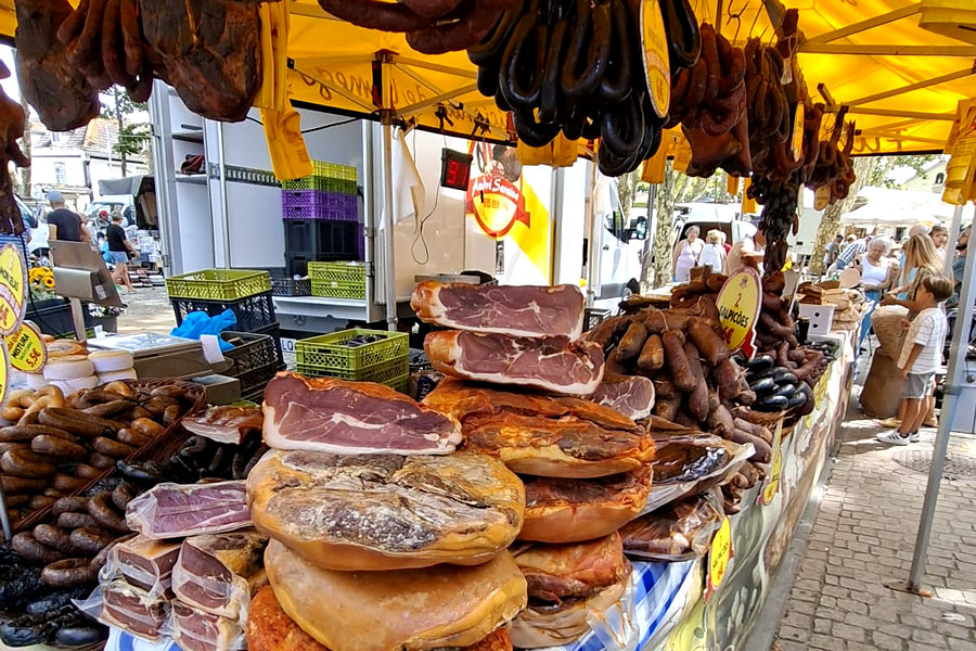Presuntos e chouriças pendurados no toldo amarelo de uma banca de fumeiro