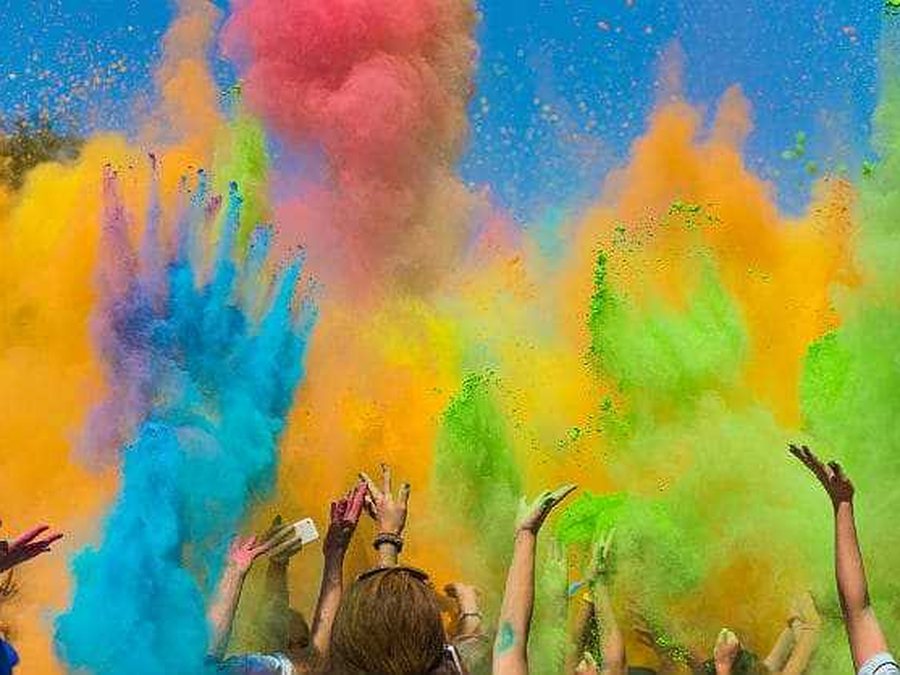 Multidão a atirar pó colorido ao ar, com as mãos levantadas, numa festa Holi
