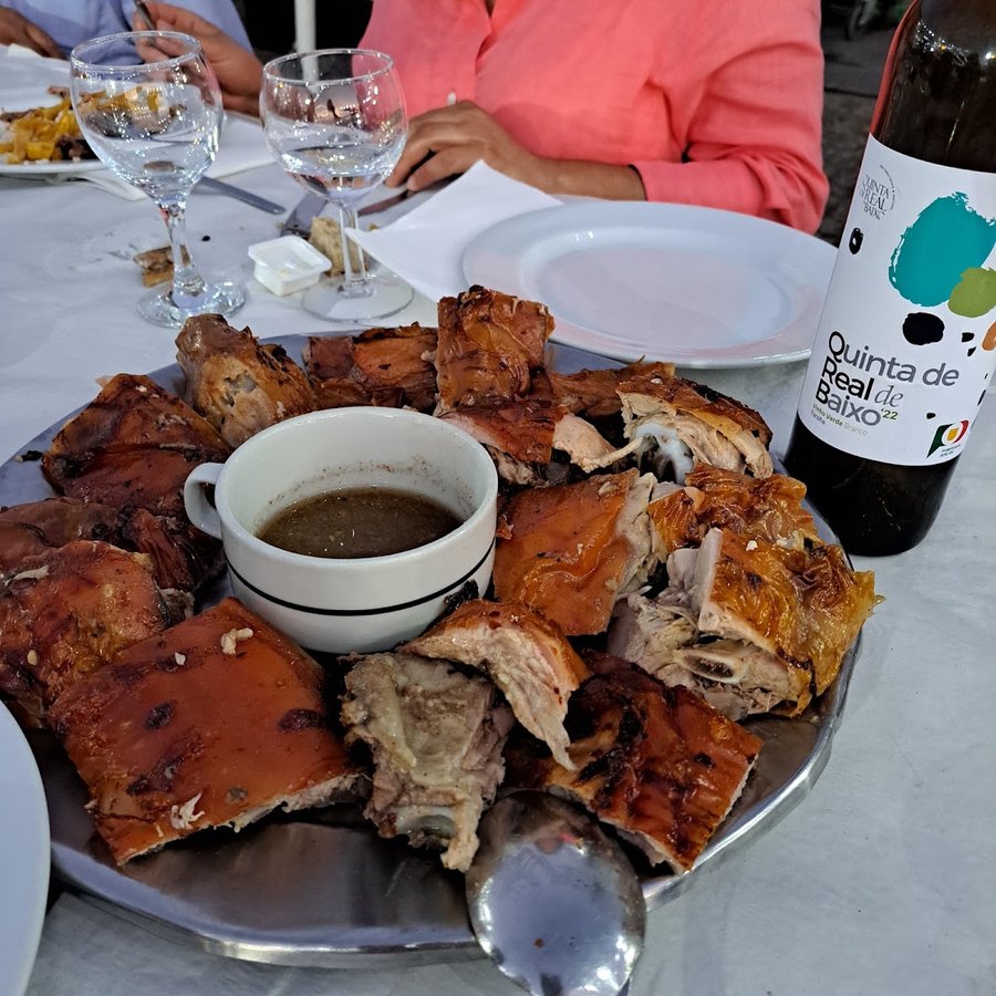 Travessa de leitão assado fatiado com molho, à mesa de pano branco no Pinheiral dos Leitões