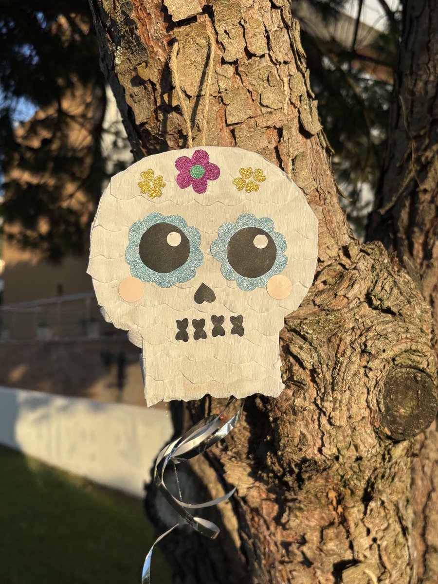 Pinhata de caveira branca com flores de purpurina e olhos azuis, pendurada numa árvore