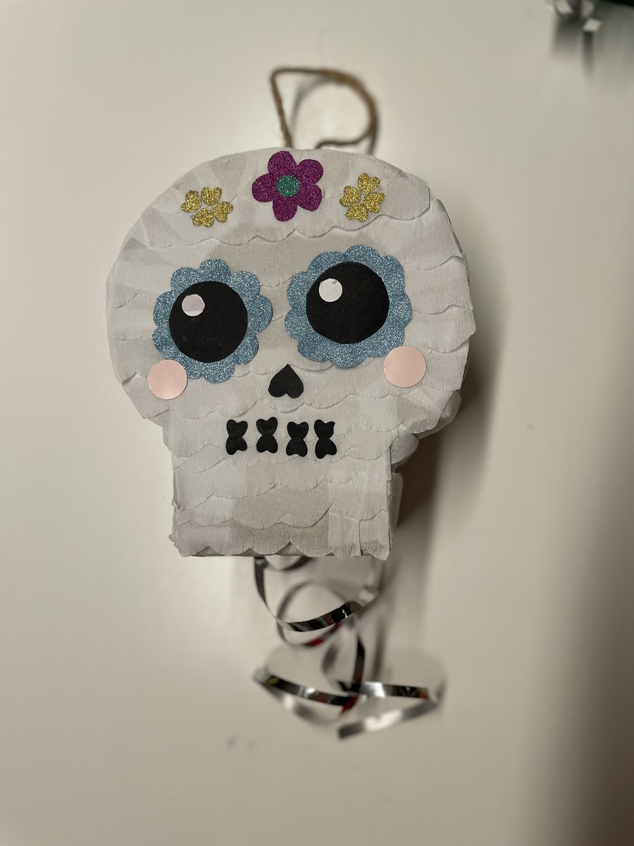 Pinhata de caveira branca com flores de purpurina, em fundo claro