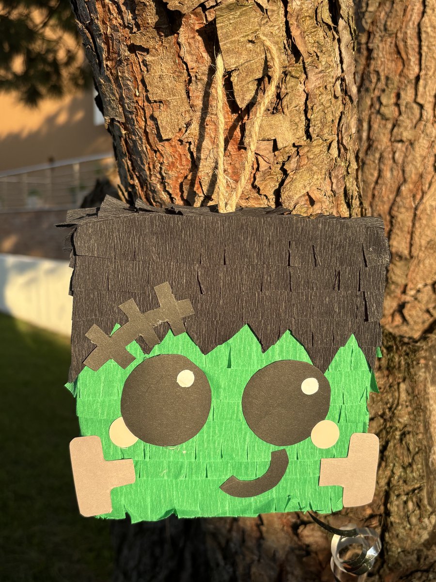 Pinhata do Frankenstein com franjas verdes e pretas, pendurada no tronco de uma árvore