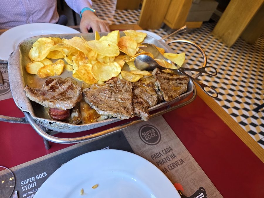 Travessa de carne grelhada com batata frita às rodelas, numa mesa do Tourigalo